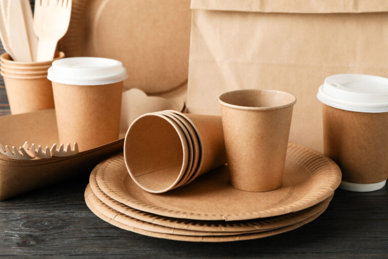 Eco - friendly tableware and paper bag on wooden table, close up