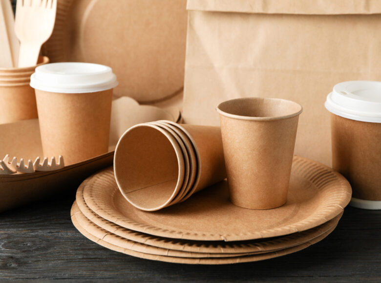 Eco - friendly tableware and paper bag on wooden table, close up